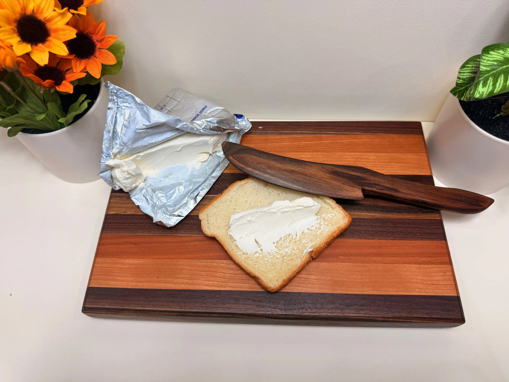Wood butter spreader beside a slice of bread with butter on a wooden board.