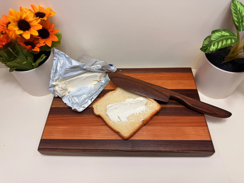 Wood butter spreader with tapered handle resting on a charcuterie board