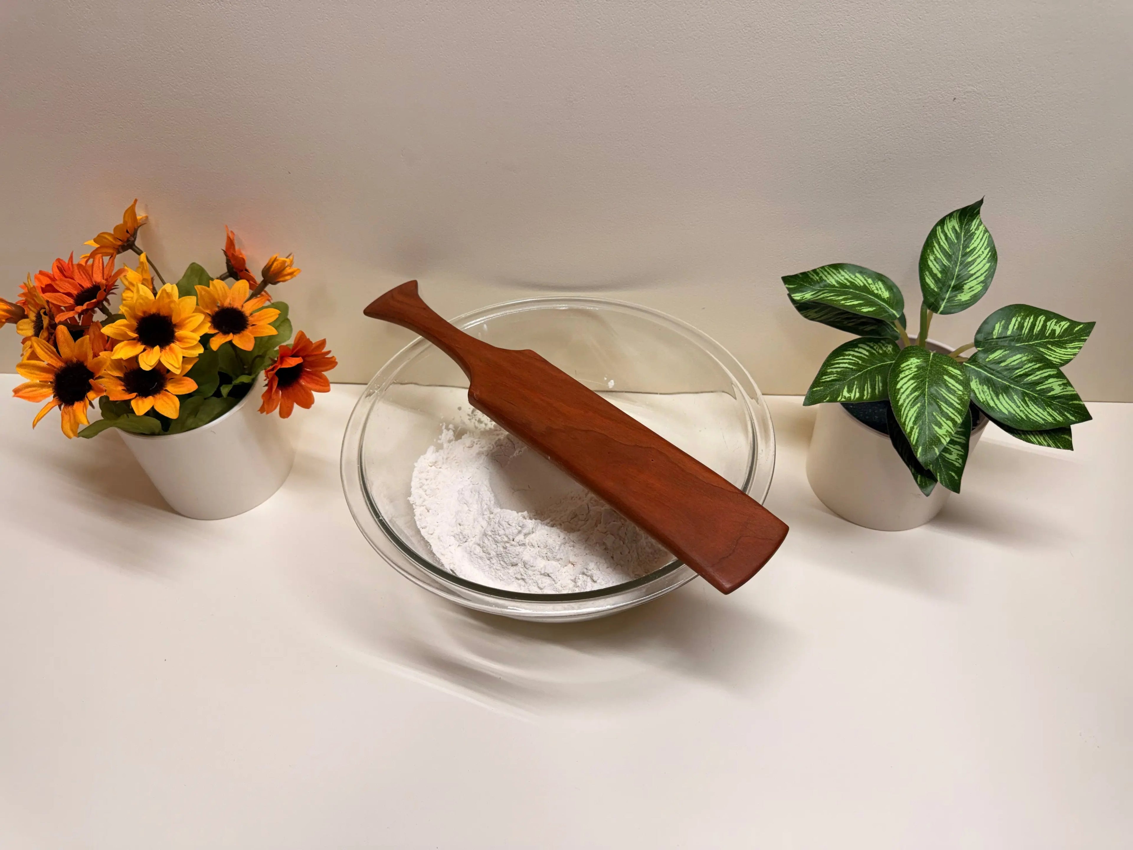 Wooden kitchen spurtle across a bowl of flour, warm brown wood.