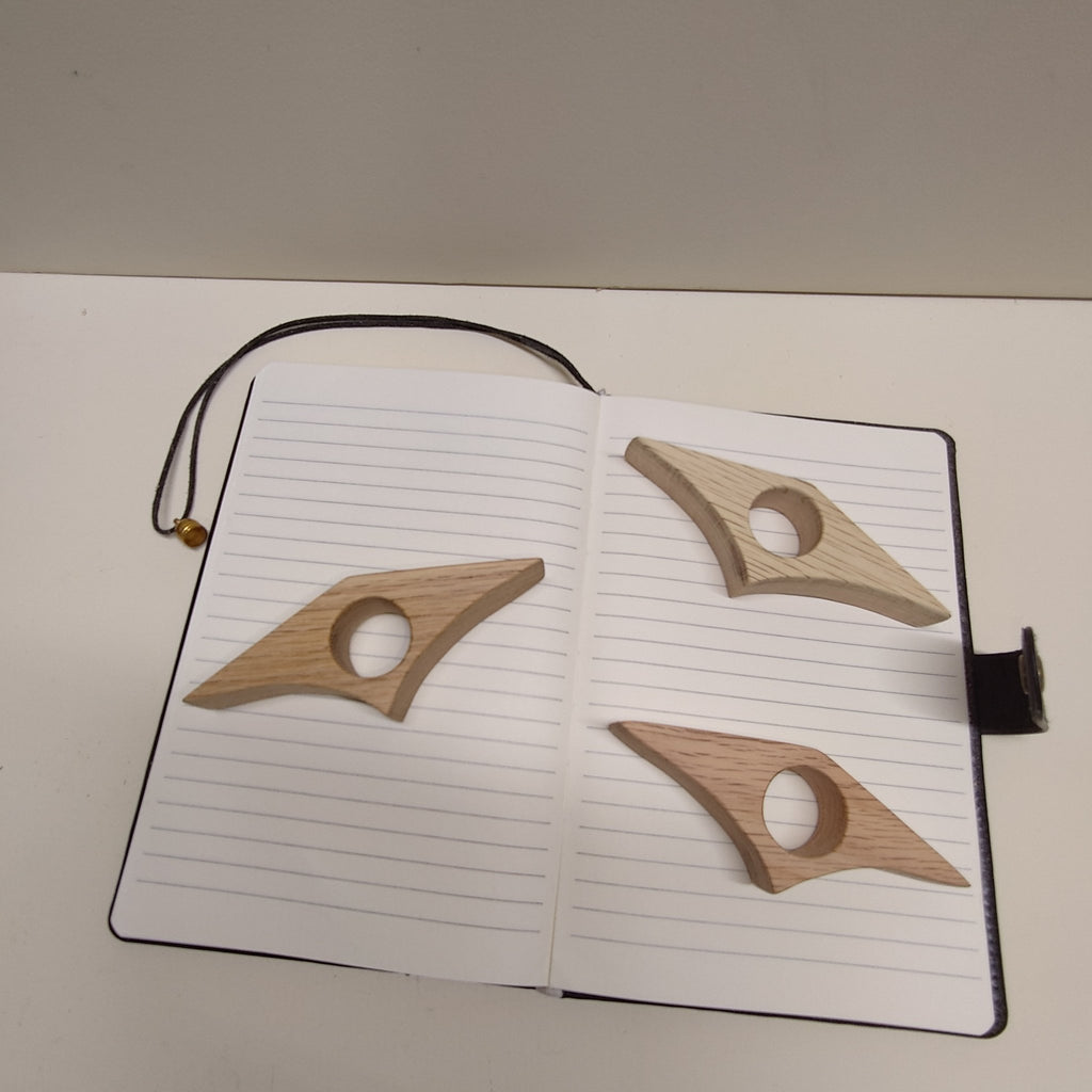 Red oak page holders: three star-shaped wooden clips on an open notebook, circular holes